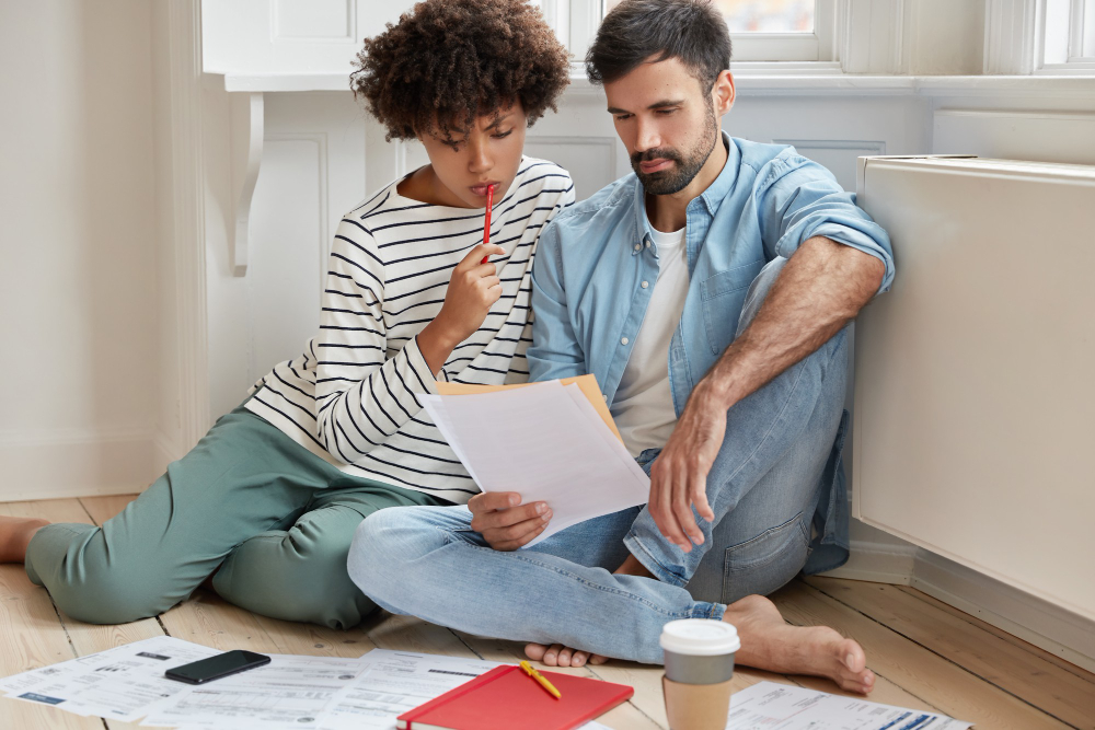 Couple sitting on the floor, reviewing paperwork together with focused expressions